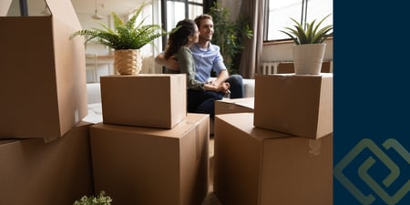 Couple sitting on the floor surrounded by boxes inside a new home after moving in.